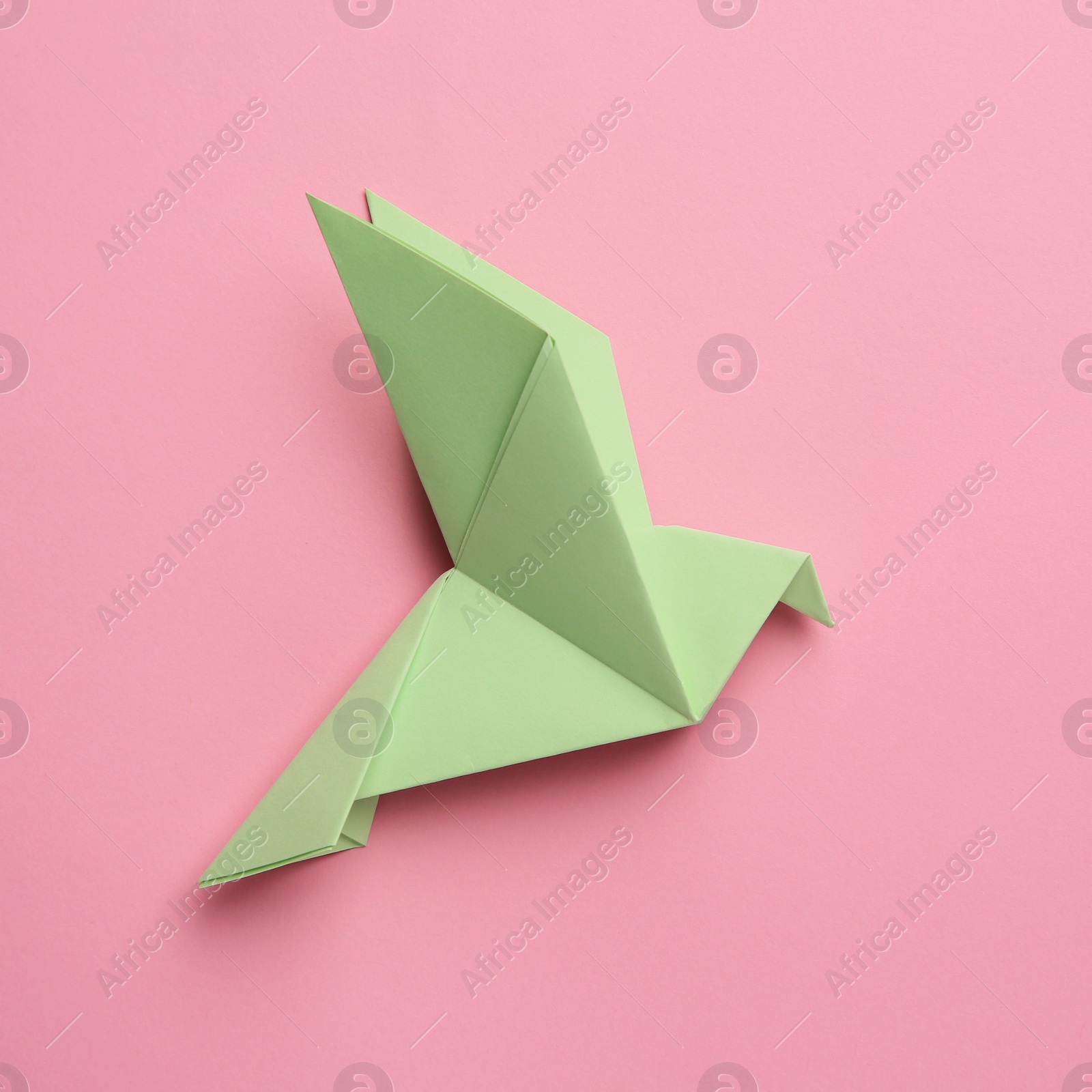 Photo of Beautiful light green origami bird on pink background, top view