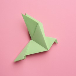 Photo of Beautiful light green origami bird on pink background, top view