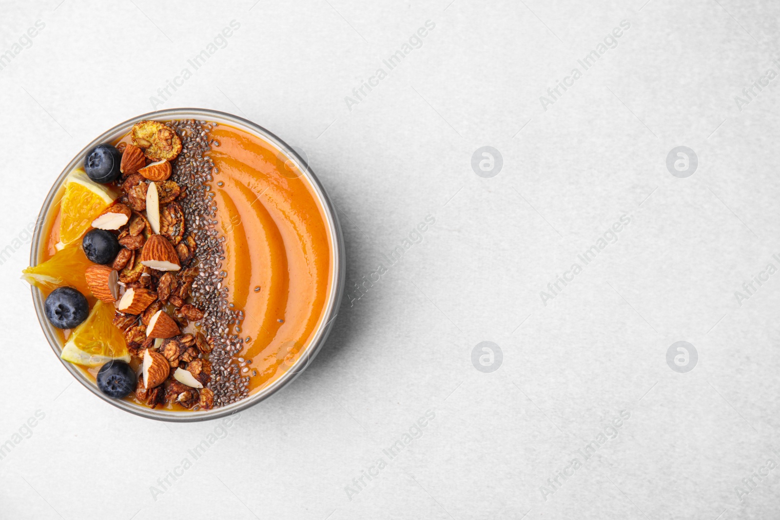 Photo of Bowl of delicious fruit smoothie with fresh orange slices, blueberries and granola on light grey background, top view. Space for text