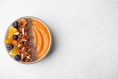 Photo of Bowl of delicious fruit smoothie with fresh orange slices, blueberries and granola on light grey background, top view. Space for text