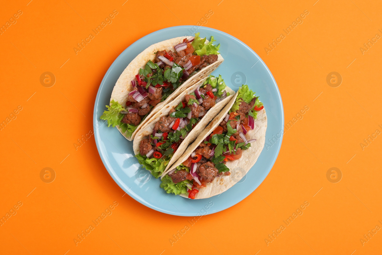 Photo of Delicious tacos with meat and vegetables on orange table, top view