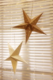 Photo of Beautiful decorative stars and festive lights hanging on window indoors. Christmas atmosphere