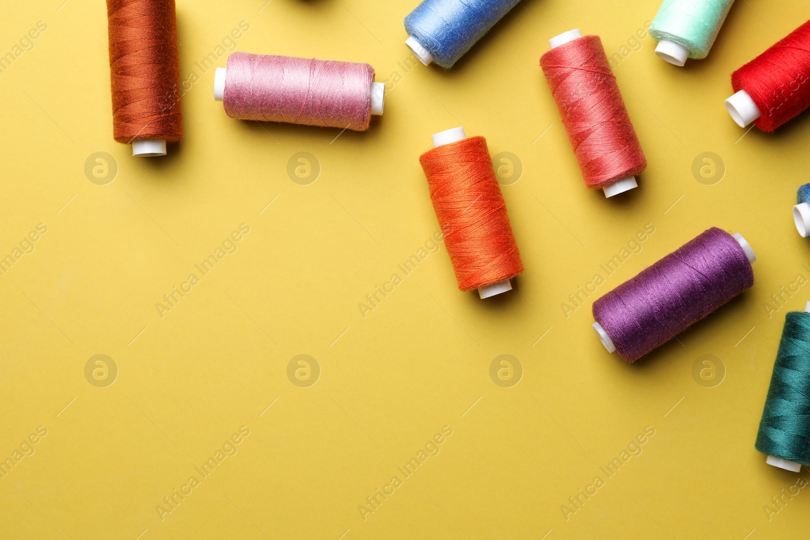 Photo of Different colorful sewing threads on yellow background, flat lay. Space for text