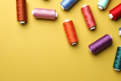 Photo of Different colorful sewing threads on yellow background, flat lay. Space for text