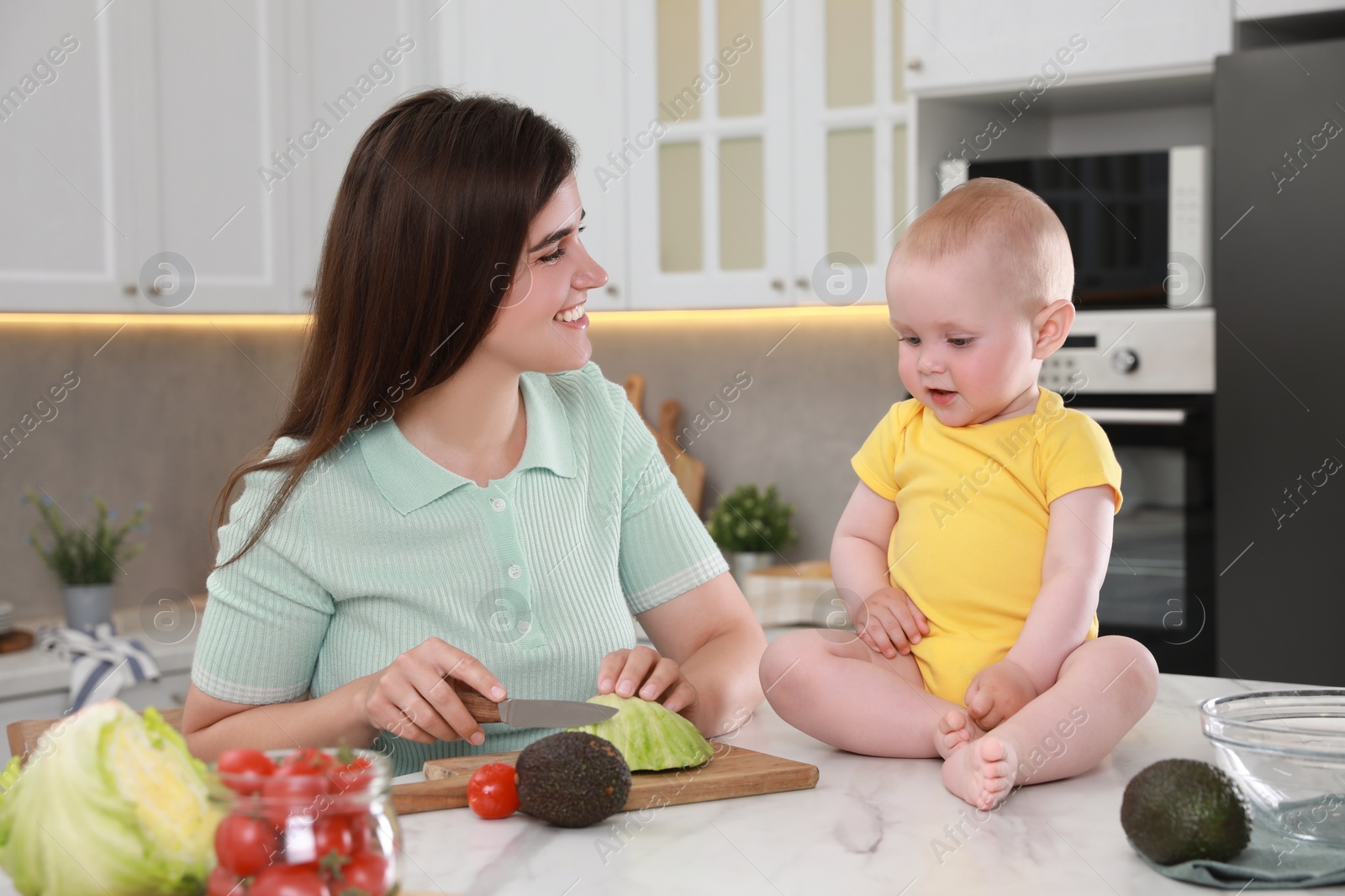 Photo of Happy young woman with her cute baby spending time together in kitchen