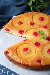 Photo of Delicious cut pineapple pie with cherry on blue table, closeup