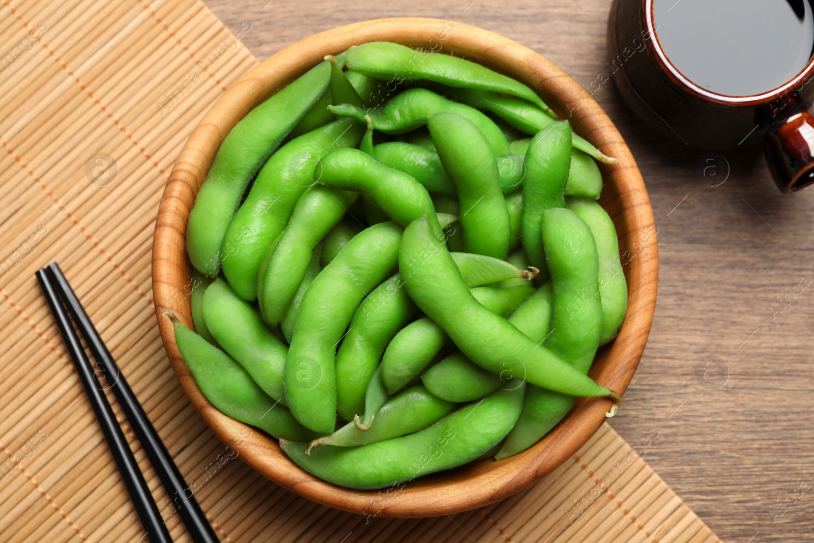 Photo of Green edamame beans in pods served with soy sauce on wooden table, flat lay