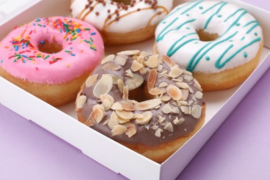 Photo of Box with different tasty glazed donuts on violet background, closeup