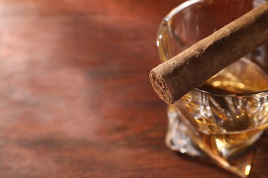 Photo of Glass of whiskey and cigar on wooden table, closeup. Space for text