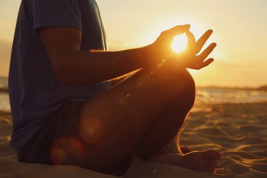 Photo of Man meditating on sandy beach at sunset, closeup
