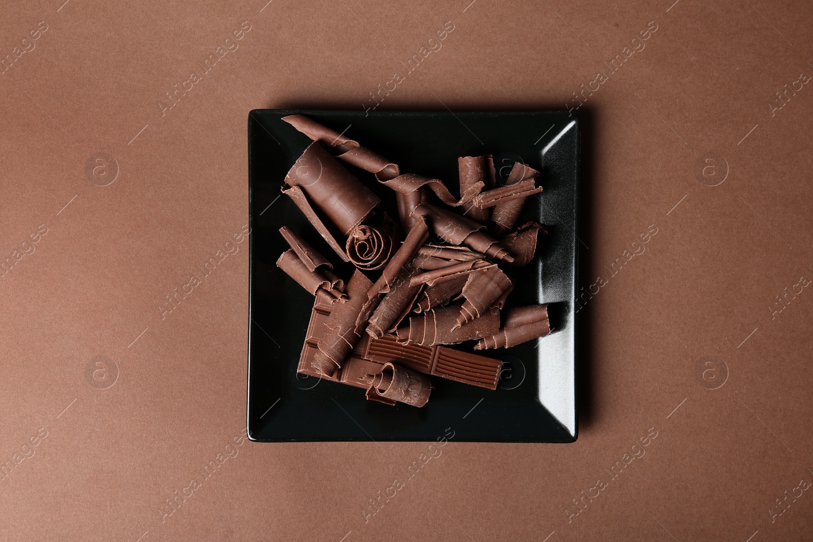 Photo of Plate with chocolate curls and pieces on color background, top view