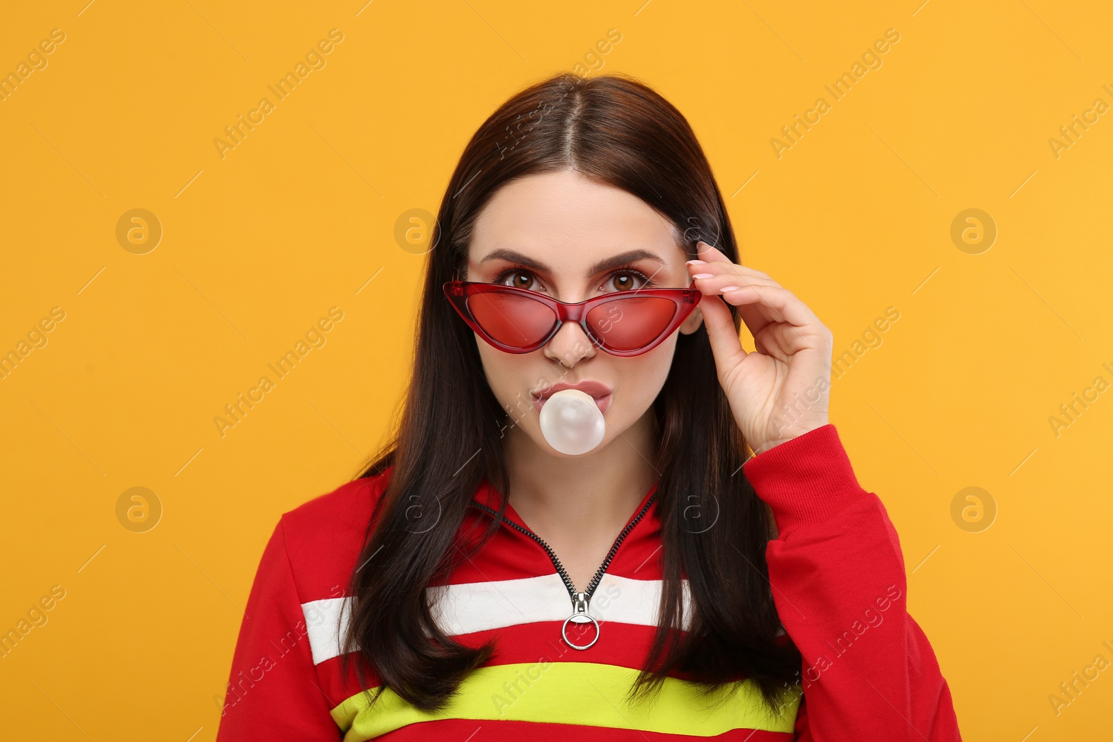 Photo of Beautiful woman in sunglasses blowing bubble gum on orange background