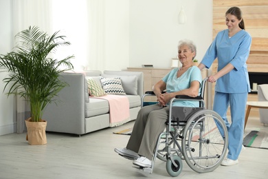 Photo of Nurse assisting elderly woman in wheelchair indoors. Space for text