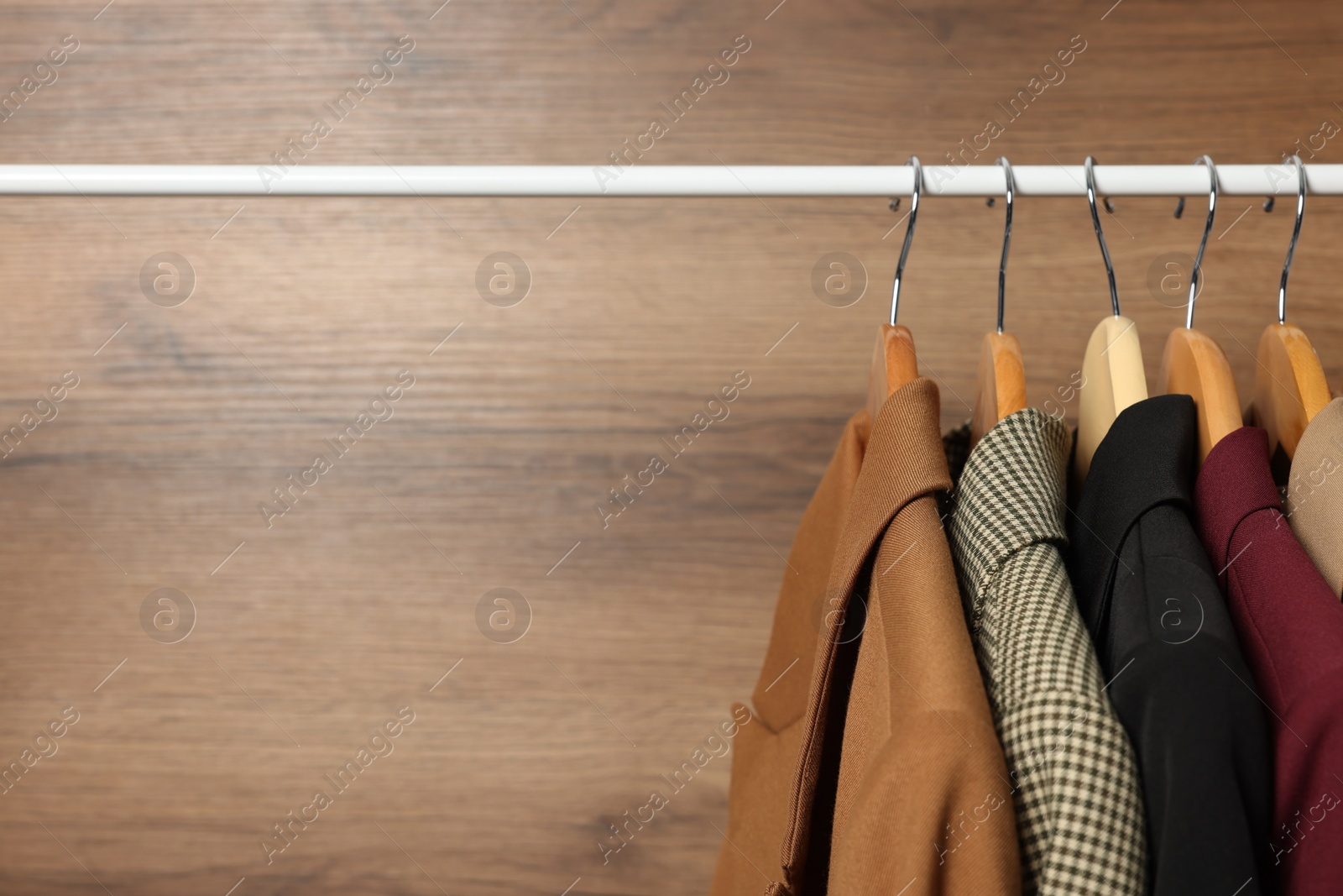 Photo of Hangers with stylish women`s clothes on rack near wooden wall, closeup. Space for text