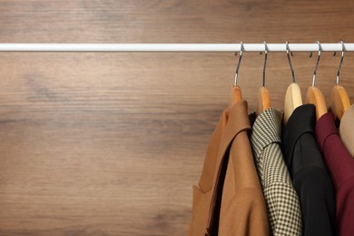 Hangers with stylish women`s clothes on rack near wooden wall, closeup. Space for text