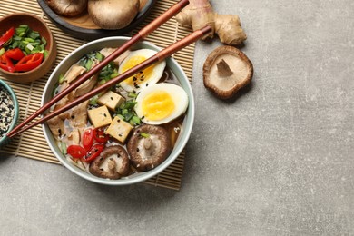 Bowl of delicious ramen and ingredients on grey table, flat lay with space for text. Noodle soup