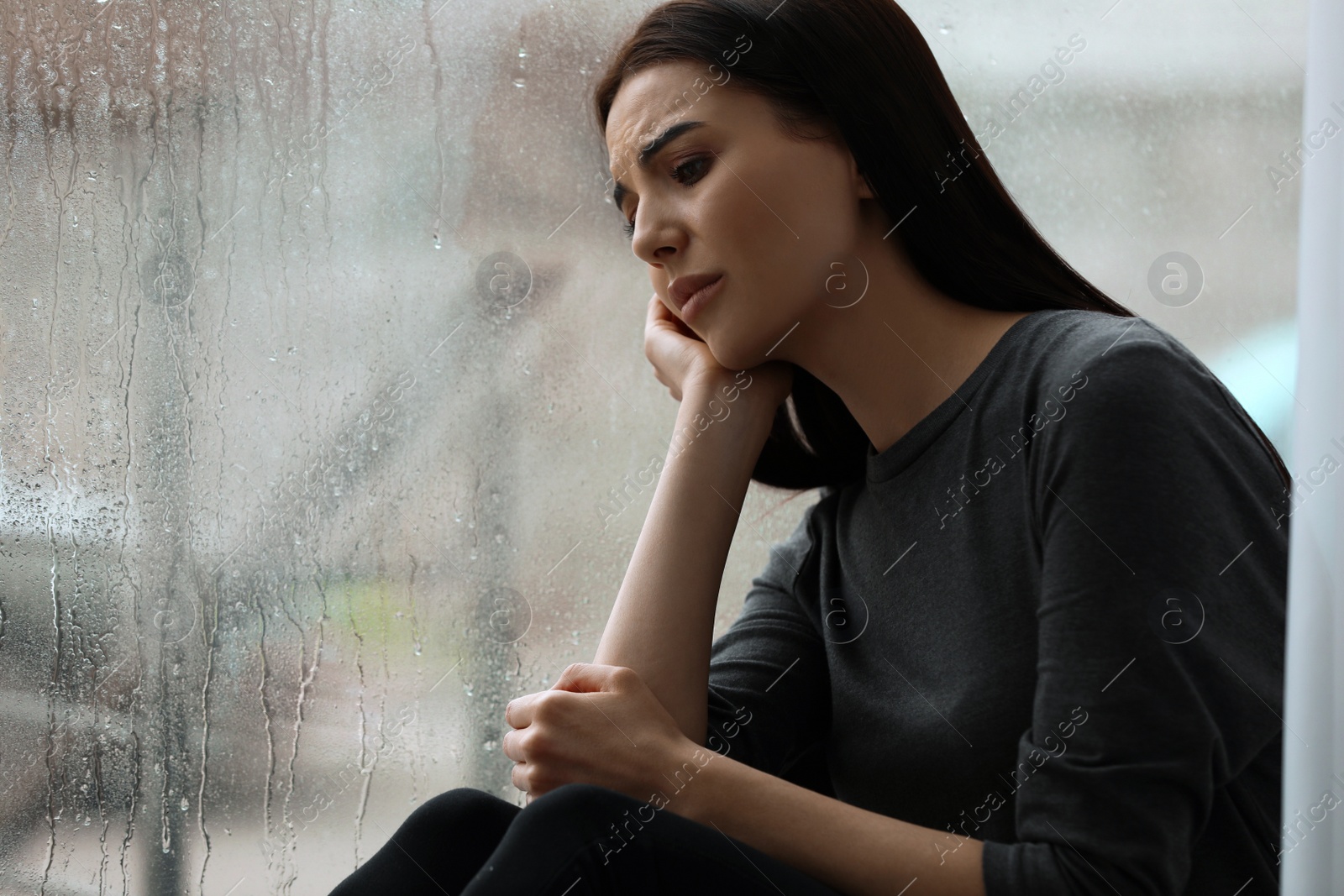 Photo of Depressed woman near window on rainy day, space for text