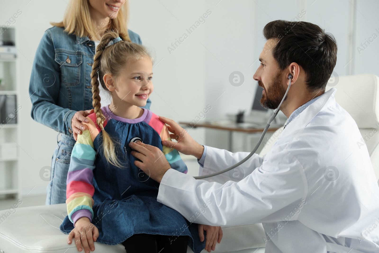 Photo of Mother and daughter having appointment with doctor. Pediatrician examining patient with stethoscope in clinic