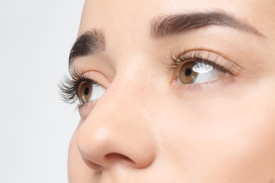 Young woman with beautiful eyelashes on light background, closeup view