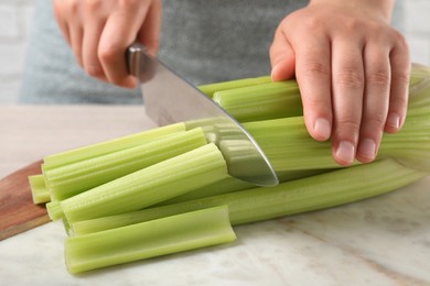 Photo of Woman cutting fresh green celery at white table indoors, closeup