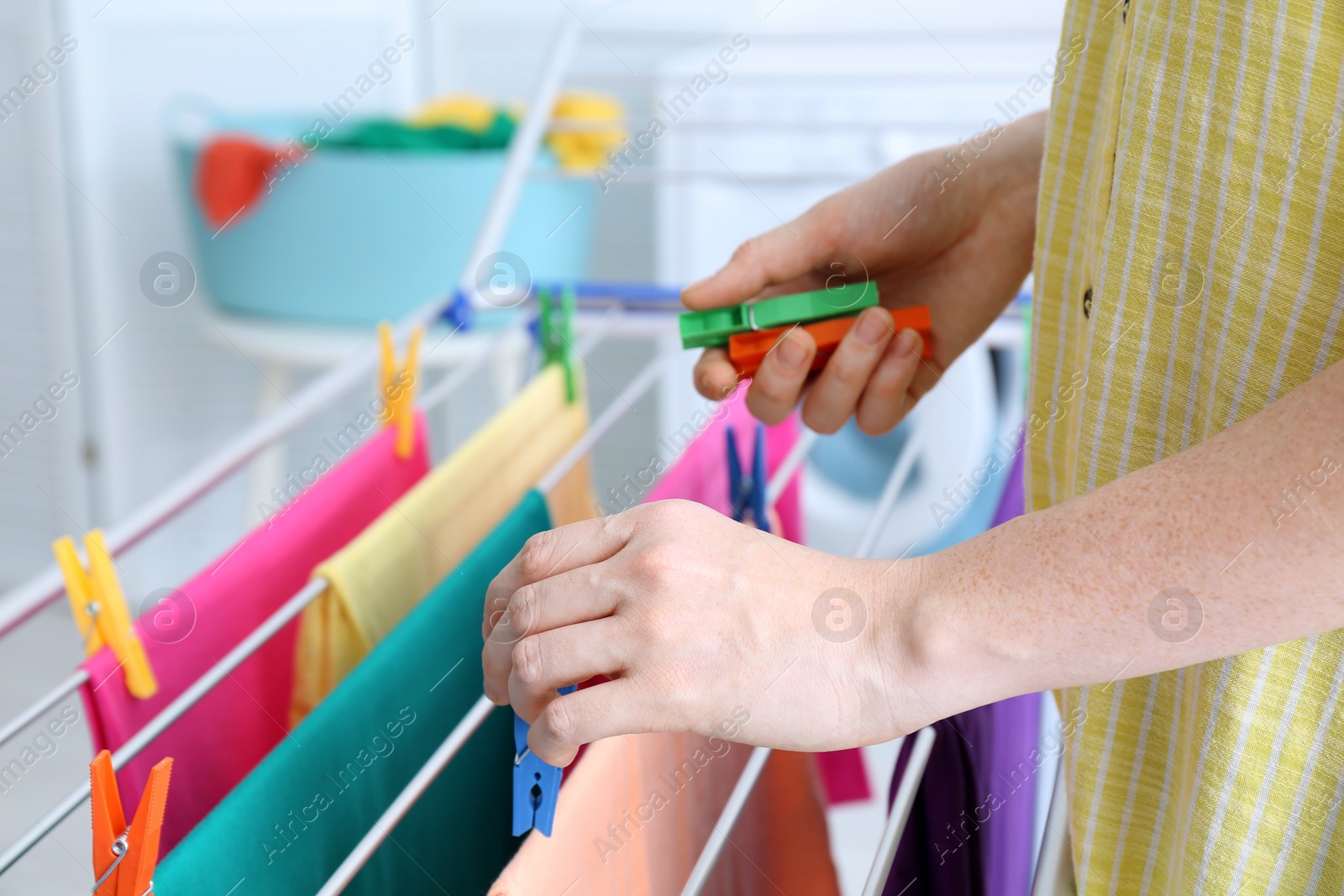 Photo of Woman hanging clean laundry on drying rack indoors, closeup