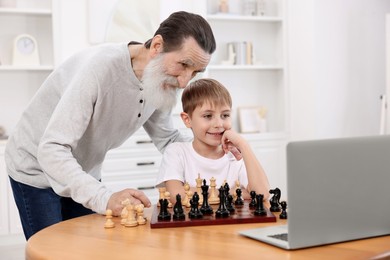 Grandfather teaching his grandson to play chess following online lesson at home