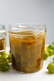 Jar of delicious gooseberry jam and fresh berries on white table, closeup