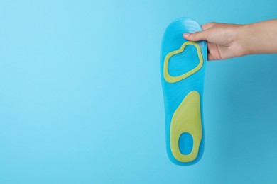 Photo of Woman holding orthopedic insole on light blue background, closeup. Space for text