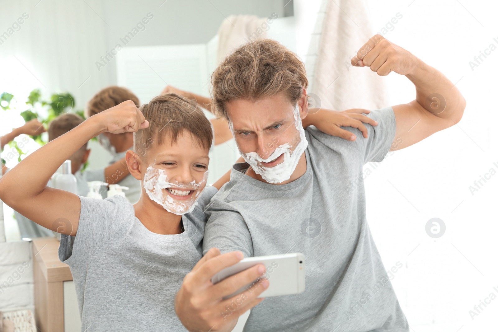 Photo of Father and son taking selfie with shaving foam on faces in bathroom