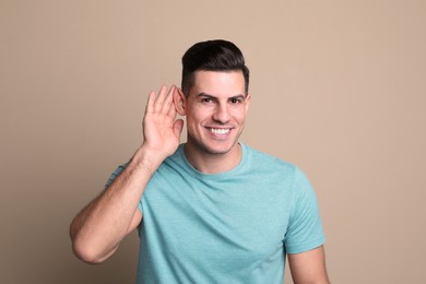 Man showing hand to ear gesture on beige background