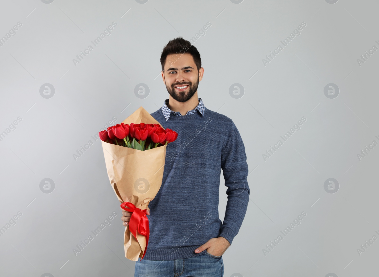 Photo of Happy man with red tulip bouquet on light grey background. 8th of March celebration
