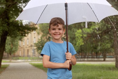 Photo of Little boy with umbrella walking under rain in park