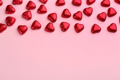 Photo of Heart shaped chocolate candies in red foil on pink background, flat lay. Space for text