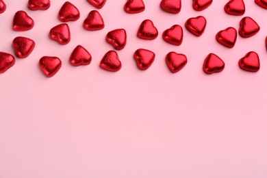 Heart shaped chocolate candies in red foil on pink background, flat lay. Space for text