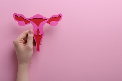 Reproductive medicine. Woman holding paper uterus on pink background, top view with space for text