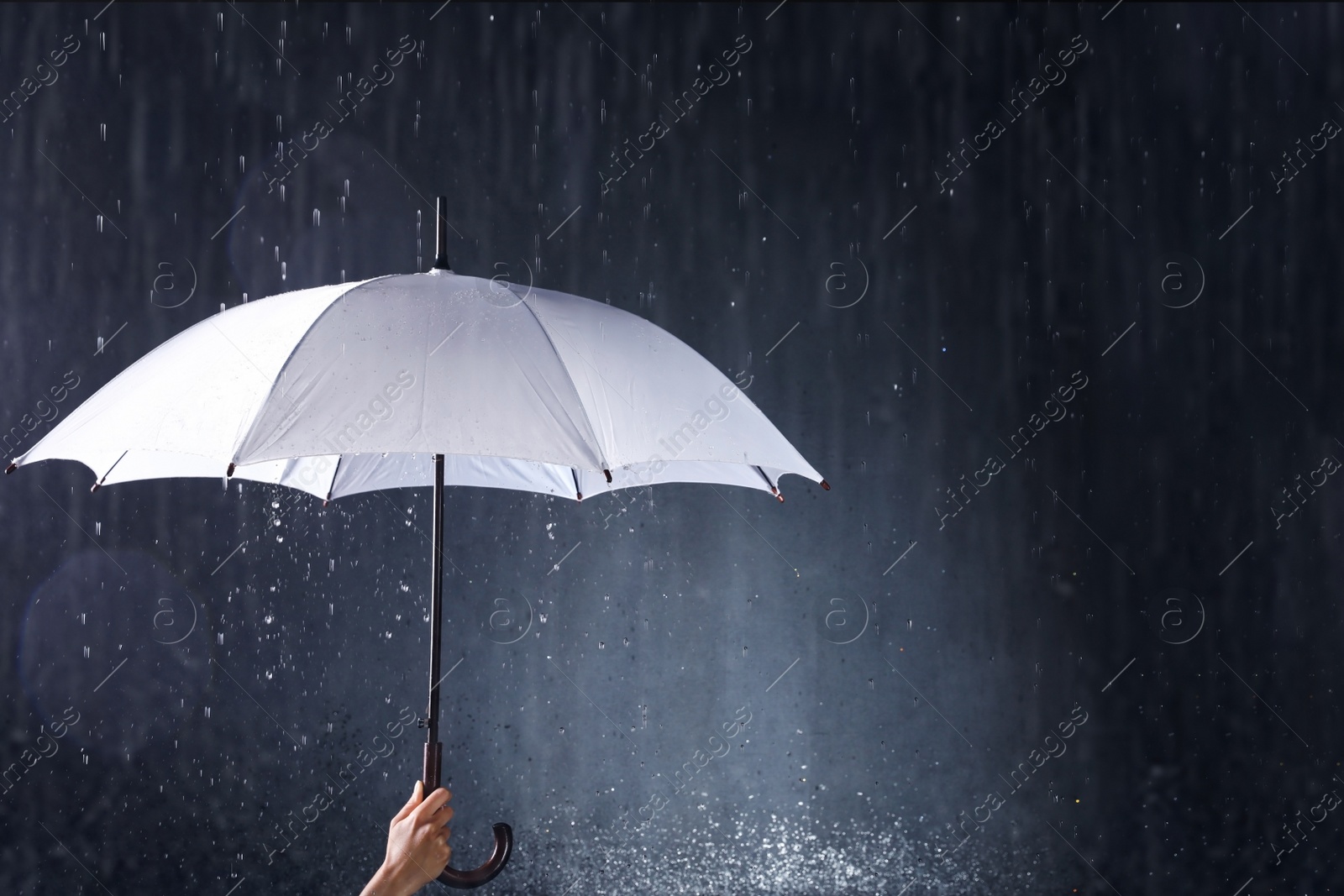 Photo of Woman holding white umbrella under rain on dark background, closeup