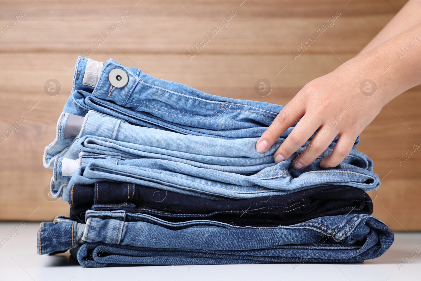 Photo of Young woman folding stylish jeans on table