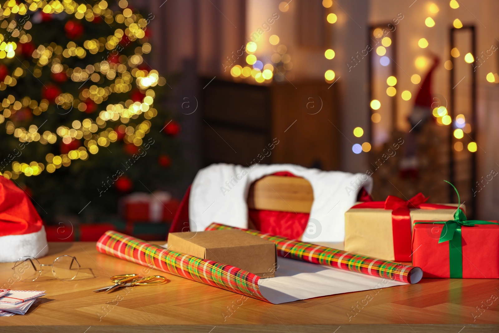 Photo of Santa's Claus workplace. Gift boxes, wrapping paper, letters on table and costume in room with Christmas decor