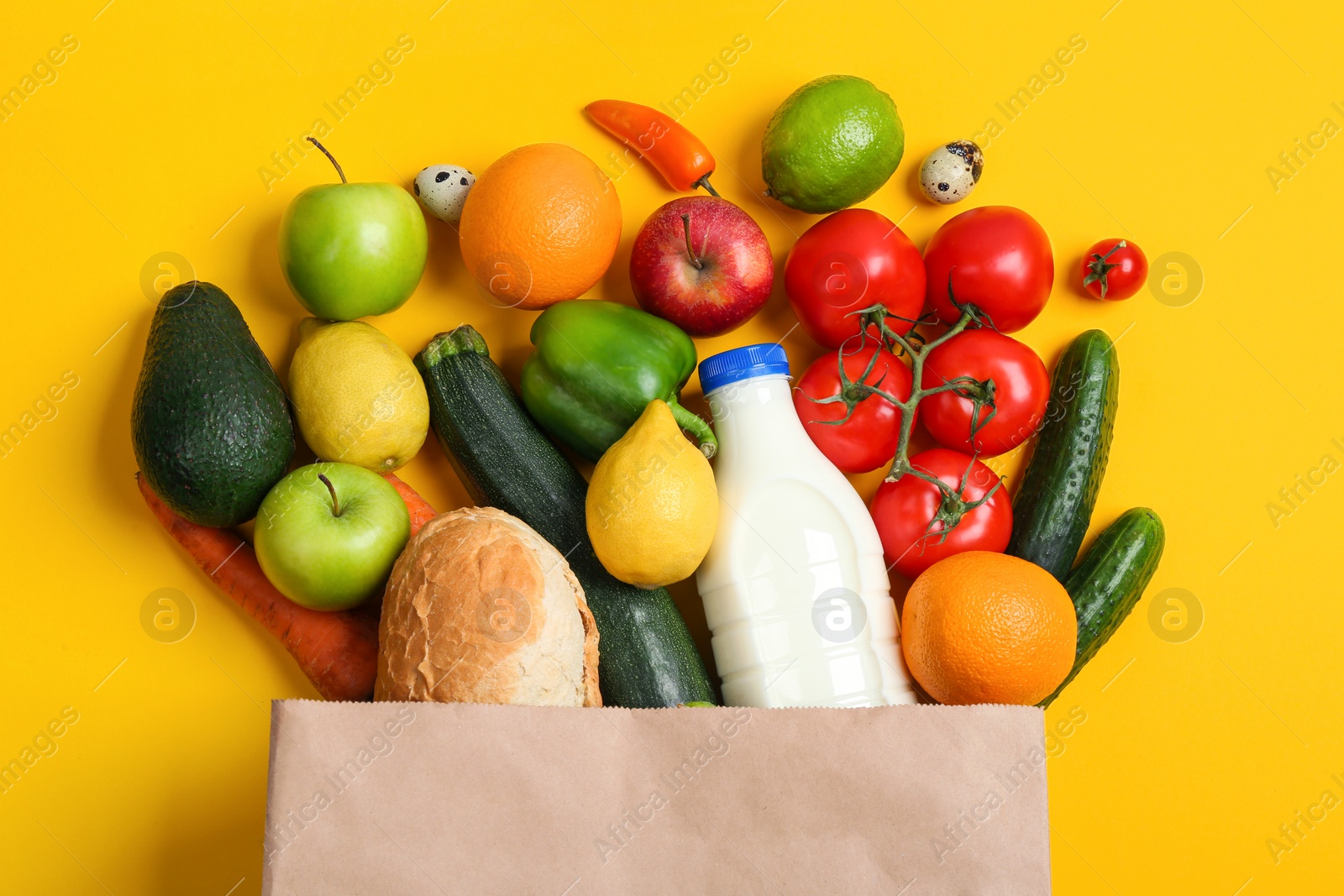 Photo of Paper bag with different groceries on yellow background, flat lay