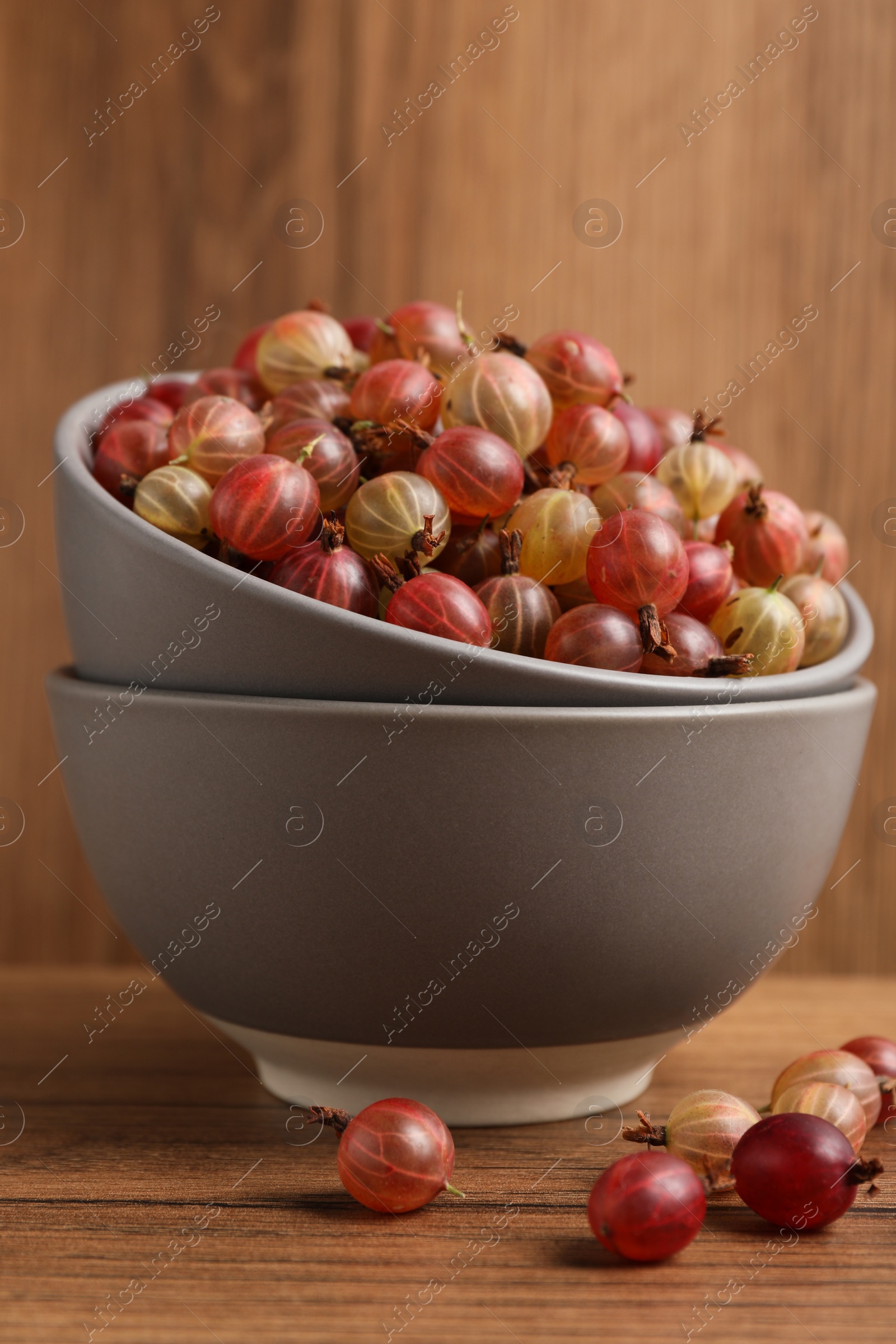 Photo of Bowls full of ripe gooseberries on wooden table