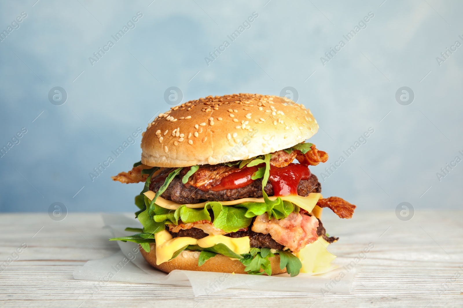 Photo of Tasty burger with bacon on table against color background