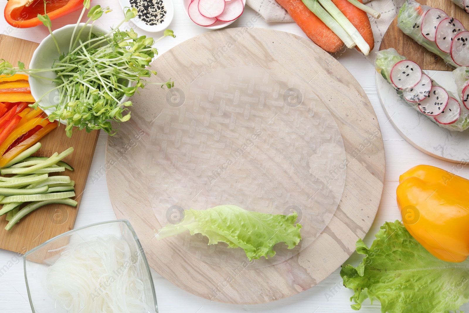 Photo of Rice paper and other ingredients for spring rolls on white wooden table, top view