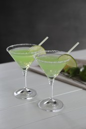 Delicious Margarita cocktail in glasses and lime on white wooden table