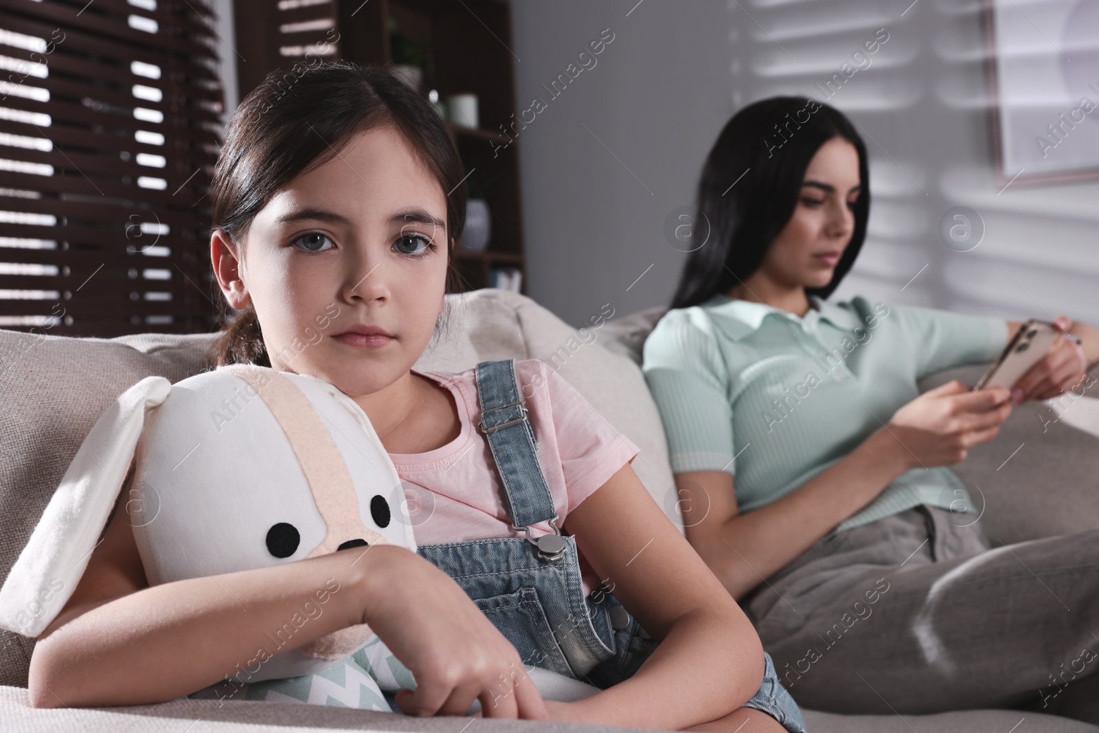 Photo of Internet addiction. Mother with smartphone ignoring her daughter in living room