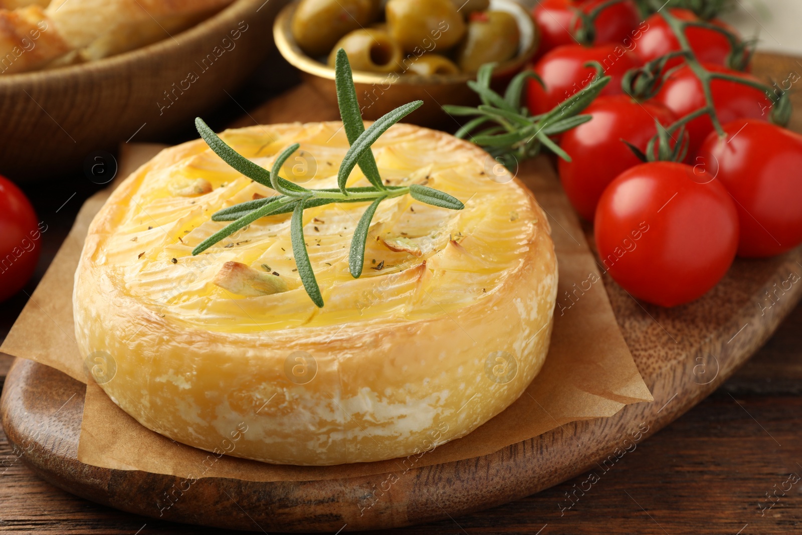 Photo of Tasty baked brie cheese with rosemary and cherry tomatoes on wooden table, closeup