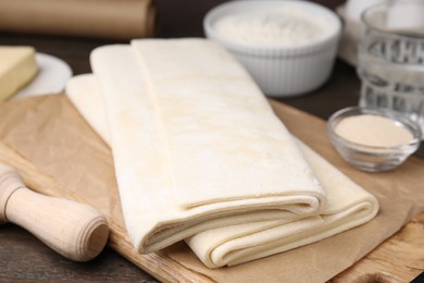 Photo of Raw puff pastry dough on wooden table, closeup