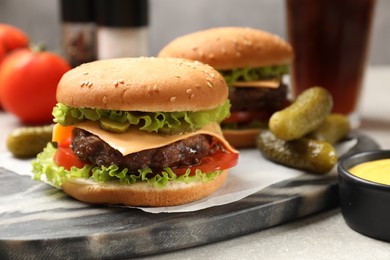 Tasty hamburgers with patties, sauce and pickles on light grey table, closeup