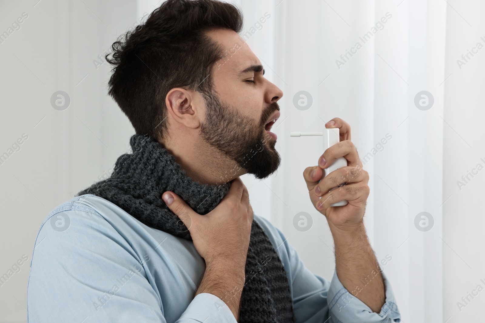 Photo of Young man with scarf using throat spray indoors