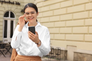 Photo of Beautiful young woman using smartphone near building outdoors