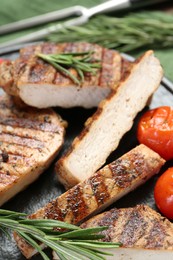 Photo of Cut grilled pork steak, rosemary and tomatoes on slate plate, closeup